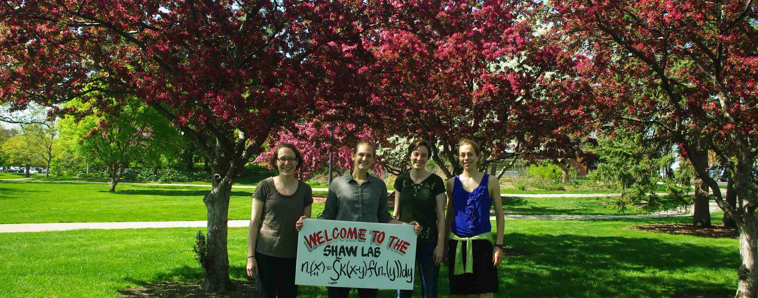 Four people holding a sign that says Welcome to the Shaw Lab
