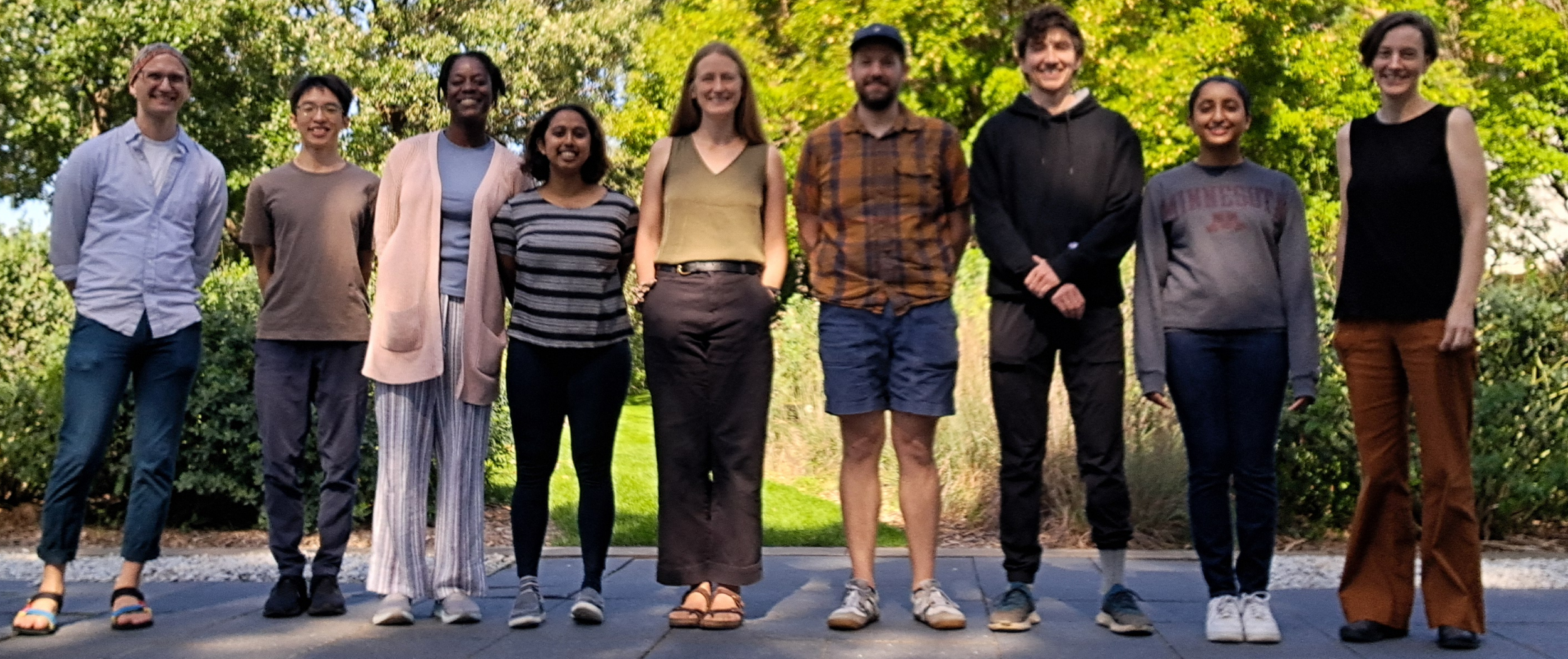Nine people standing outside on a walk way with vegetation in the background
